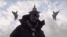 a man wearing a mask is standing in front of two fighter jets in the sky .