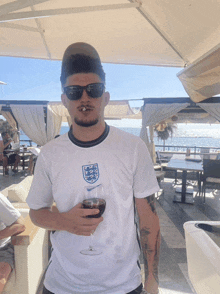 a man holding a glass of wine wearing a shirt that says england