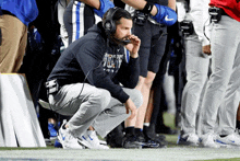 a man wearing headphones and a sweatshirt that says duke is kneeling on the field