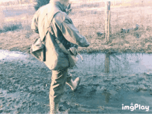 a man in a military uniform is walking through a muddy area with a watermark that says imgplay on the bottom