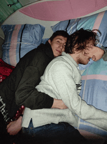 two men laying on a bed with one wearing a sweater with the letter n on it