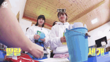 a group of girls are standing around a table with a blue bucket in front of them with korean writing on it