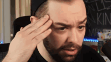 a man with a beard holds his hand to his forehead in front of a blackboard that says mr. king