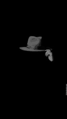 a black and white photo of a person 's hand holding a hat in the dark .