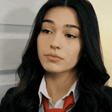 a woman wearing a white shirt and red tie looks at the camera