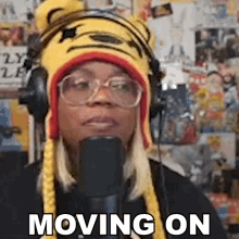 a woman wearing a tiger hat and headphones is talking into a microphone and says moving on .