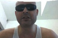 a man wearing sunglasses and a white tank top looks at the camera