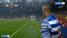 a man wearing a blue and white striped shirt with the word shiba on it stands on a soccer field