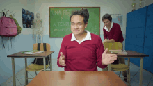 a boy in a red sweater sits at a desk in front of a green board that says una paja y a dorm