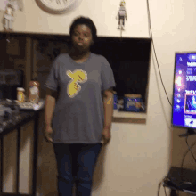 a woman wearing a peanuts shirt stands in front of a tv screen