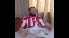 a man wearing a red and white adidas shirt is sitting at a table with a bowl and spoon .