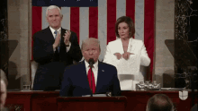 a man in a suit and tie is giving a speech while a woman holds a piece of paper in front of him