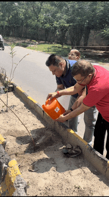 a man in a red shirt is watering a plant with an orange bucket