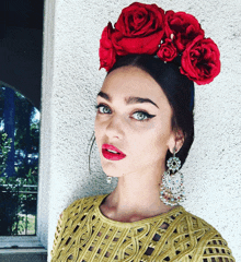 a woman wearing a yellow top and earrings has red flowers in her hair