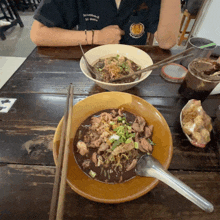 a person sitting at a table with a bowl of food and a bowl of soup with chopsticks in it