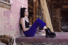 a woman in a black top and blue pants sits on the ground