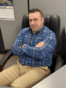 a man in a blue plaid shirt sits in a chair with his arms crossed in front of a calendar for january 2020