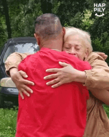 a man in a red shirt is hugging a woman in front of a car with hap pily written on the bottom