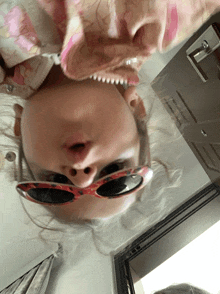 a girl wearing sunglasses is upside down and making a face