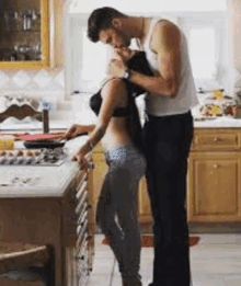 a man and a woman are kissing in a kitchen . the woman is wearing a bra .