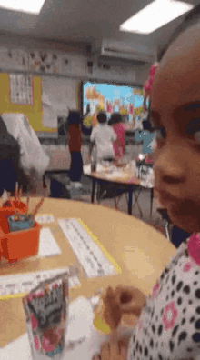 a little girl is sitting at a table in a classroom with a bag of s'mores in front of her