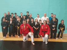 a group of people posing for a picture with one man wearing a red shirt that says ' karate ' on it