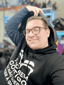 a man wearing glasses and a black sweatshirt that says " sem coito " is smiling