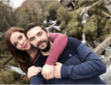 a man and a woman are posing for a picture in front of a waterfall