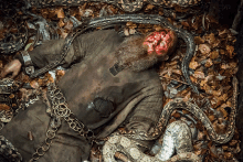 a man with a beard is chained to a snake and has blood on his face