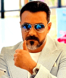 a man with a beard wearing sunglasses and a watch gives a thumbs up