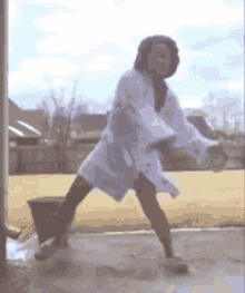 a woman in a white robe is dancing in front of a bucket .