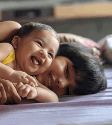 a baby and a child are laying on a bed and laughing