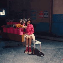 a woman in a pink shirt sits on a chair in front of a sign that says we are here