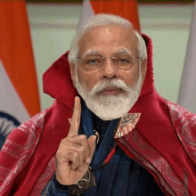 a man with a beard and glasses is wearing a red cape and pointing at the camera .