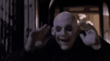 a bald man with a purple mask on his face is waving his hands .