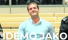 a man in a blue sweater stands in front of the word demo jako