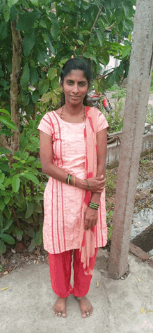 a woman in a pink dress stands in front of a tree