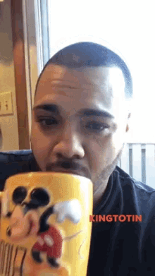 a man drinking from a mickey mouse mug with kingtotin written on it