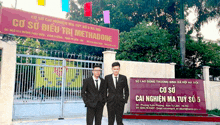 two men in suits stand in front of a sign that says co so cai nghien ma tuy so 5