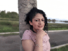 a woman with curly hair leans against a tree trunk