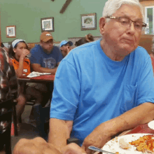 a man in a blue shirt is sitting at a table with a plate of food in front of him