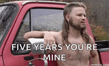 a shirtless man with a mullet is leaning on the back of a red truck and smoking a cigarette .