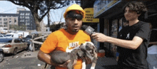 a man wearing an orange nike shirt is holding two puppies