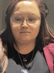 a woman wearing glasses and a necklace with a heart shaped pendant looks at the camera