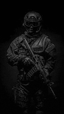 a black and white photo of a swat officer holding a gun in a dark room .