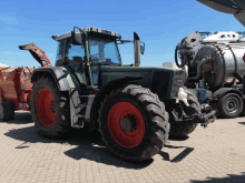 a green tractor with red tires is parked next to a silver tank