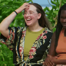 a woman in a floral kimono is laughing while standing next to another woman in an orange tank top .