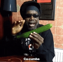 a man wearing sunglasses and a hat is holding a cucumber and says cu-cumba on the bottom