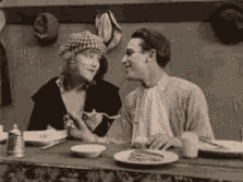 a black and white photo of a man and a woman sitting at a table with plates of food .