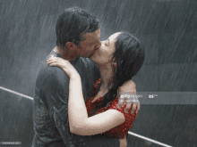 a man and a woman are kissing in the rain and the woman is wearing a red polka dot dress